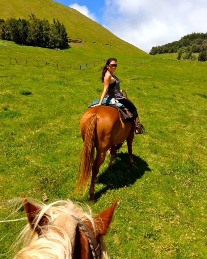 Elyssa on horseback with another horse behind her on a grassy rolling hill