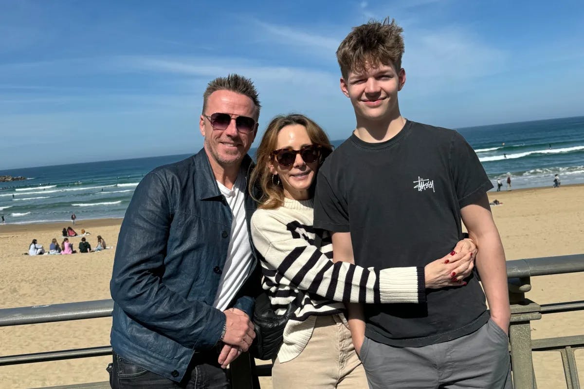 a woman in a striped sweater stands with two men at the beach