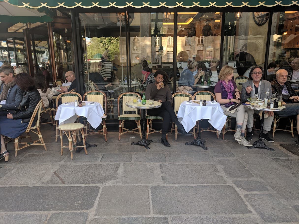 People dining on tables and chairs on a city street in front of windows and under a balcony
