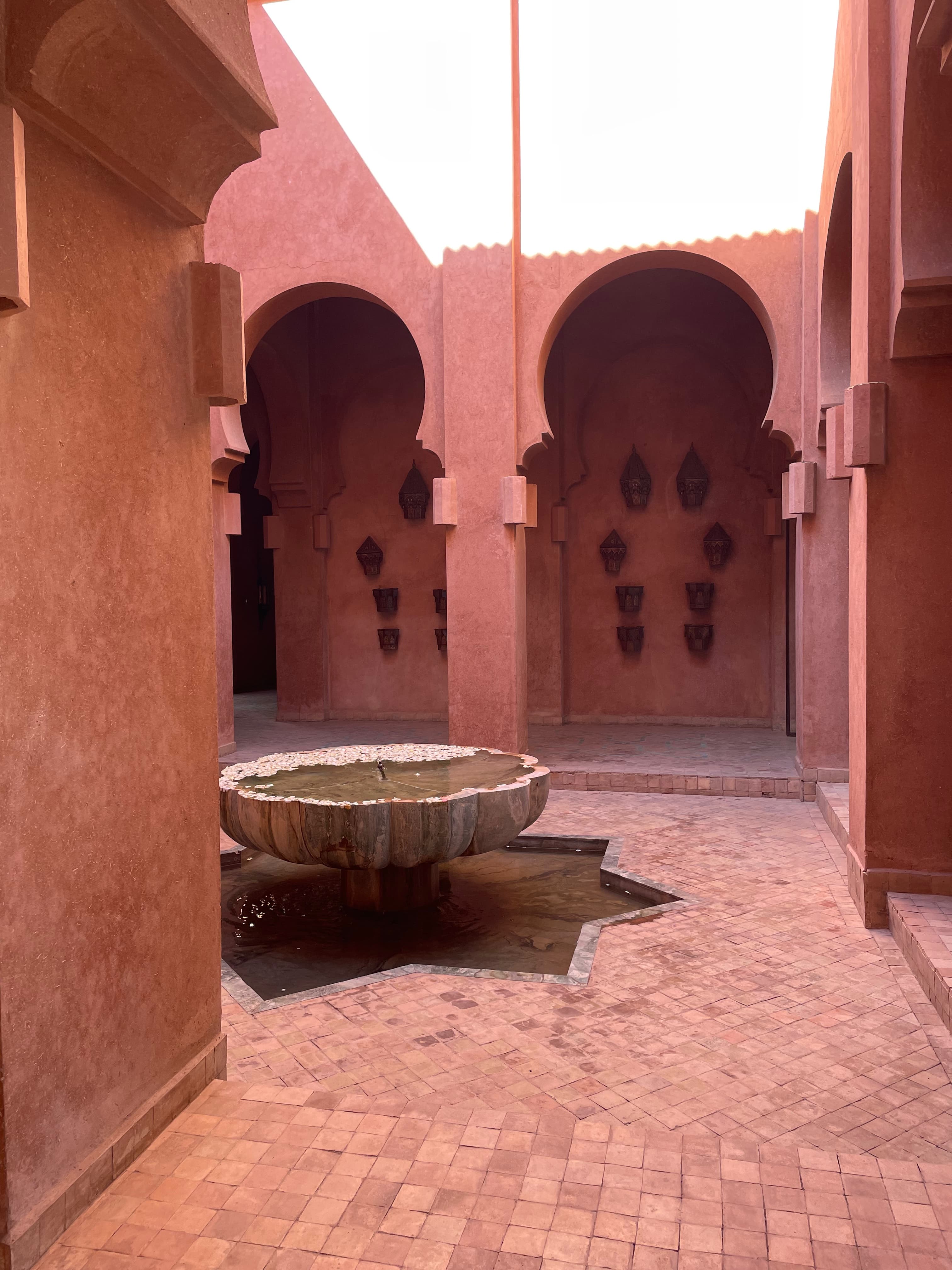 A red brick courtyard with red walls and a fountain in the center on day 2 of a Morocco 7 day itinerary.