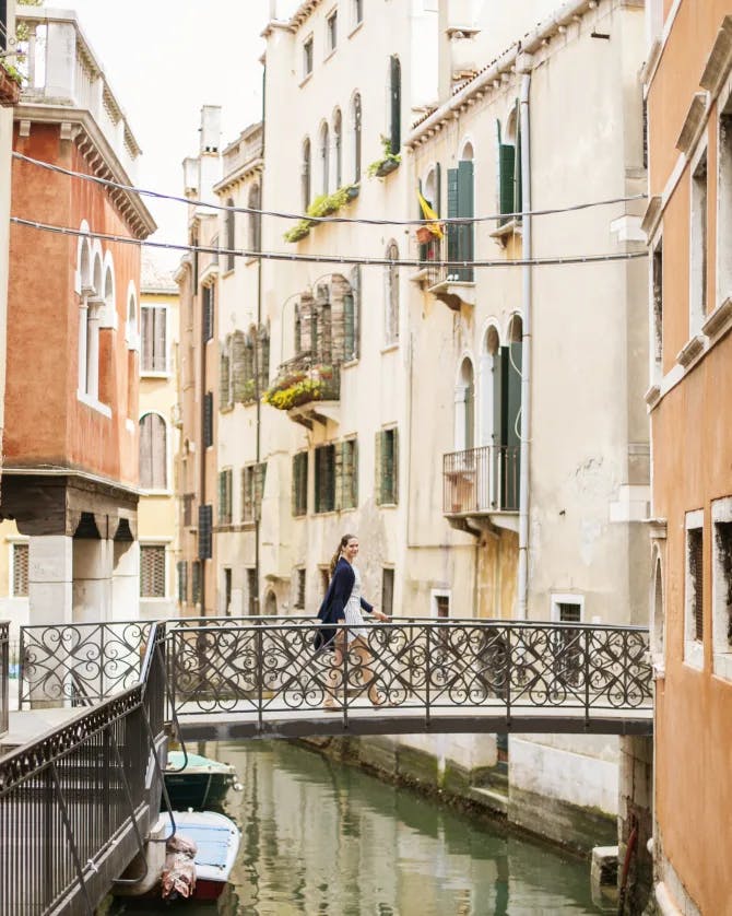 A person walking on a bridge overlooking a Venice canal with colorful buildings on each side