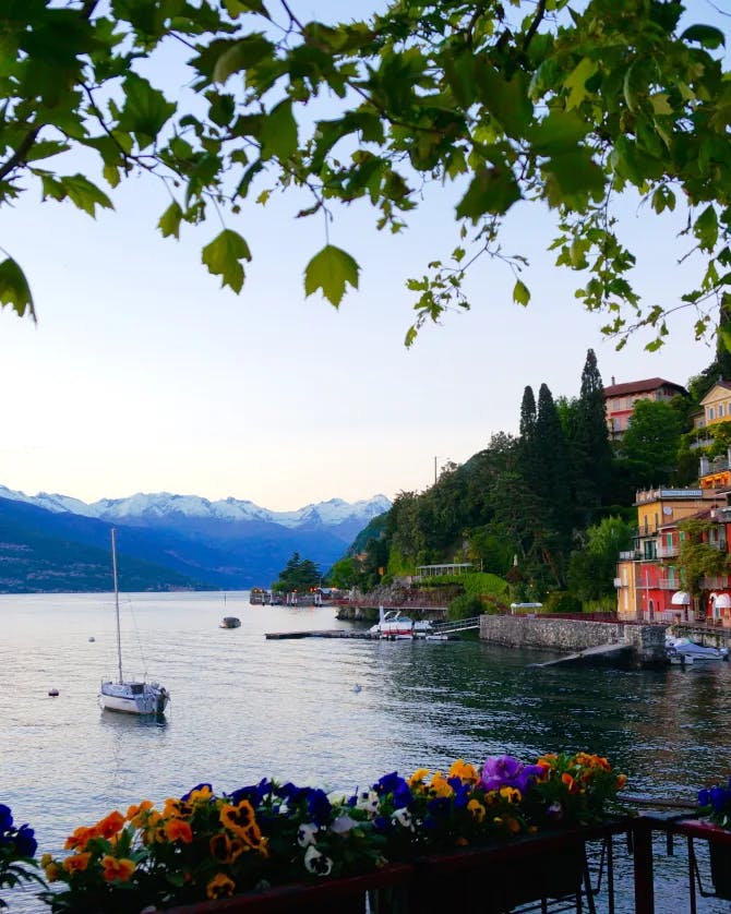 A view of Lake Como from a floral terrace with a boat, mountains and colorful neighborhood in the distance