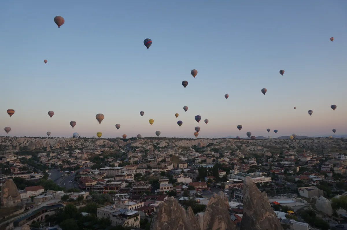 An aerial view of a city with numerous hot air balloons in the sky