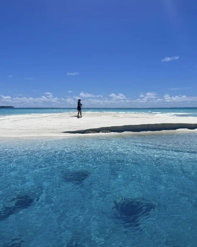 A person standing on a white sand bank surrounded by crystal clear blue water.