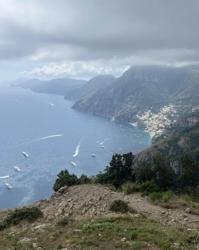 An aerial view of the Amalfi Coast with a dirt path, mountain range and sea in the distance