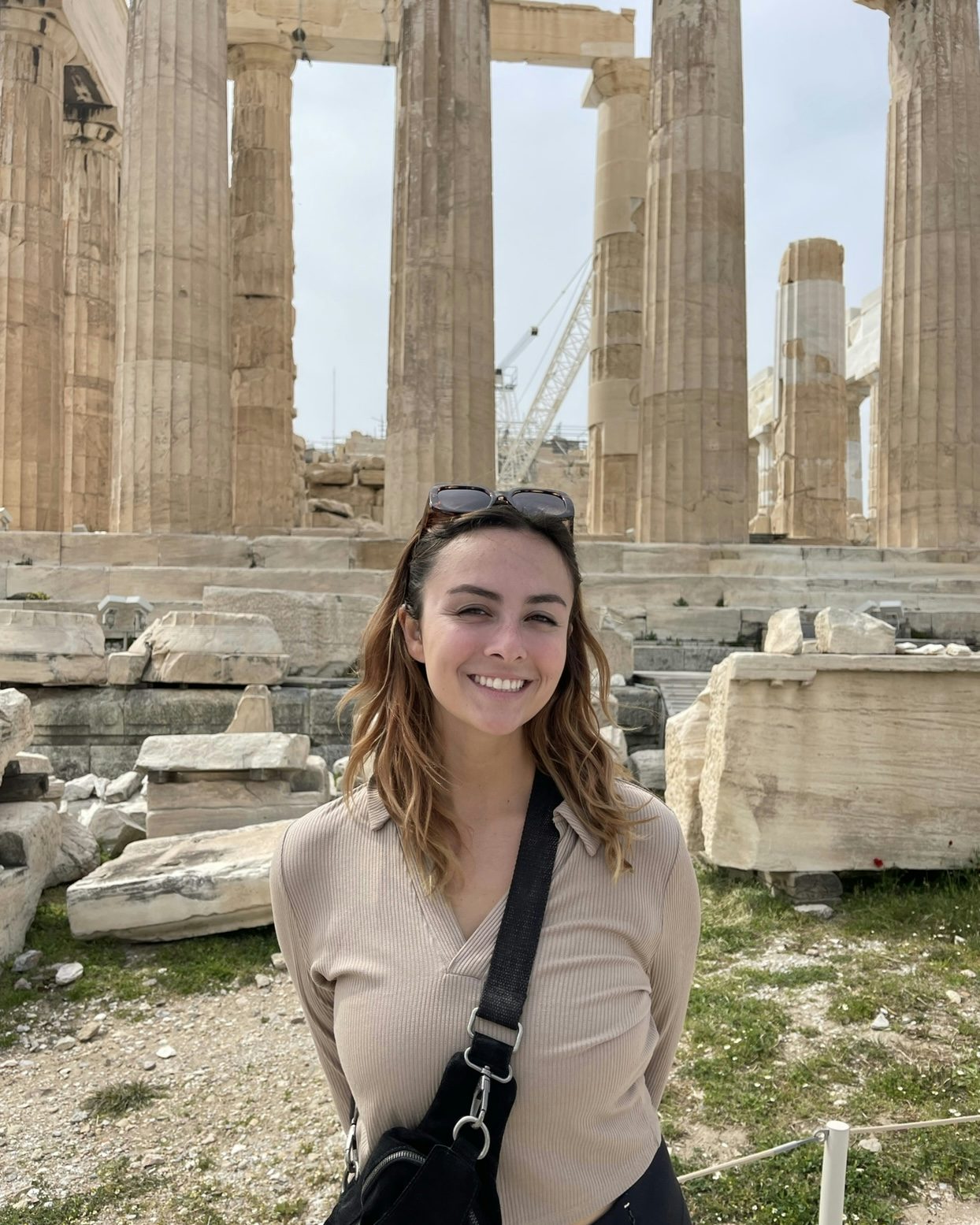Travel Advisor Olivia Lofstad in a tan shirt with a black crossbody bag in front of ancient ruins.