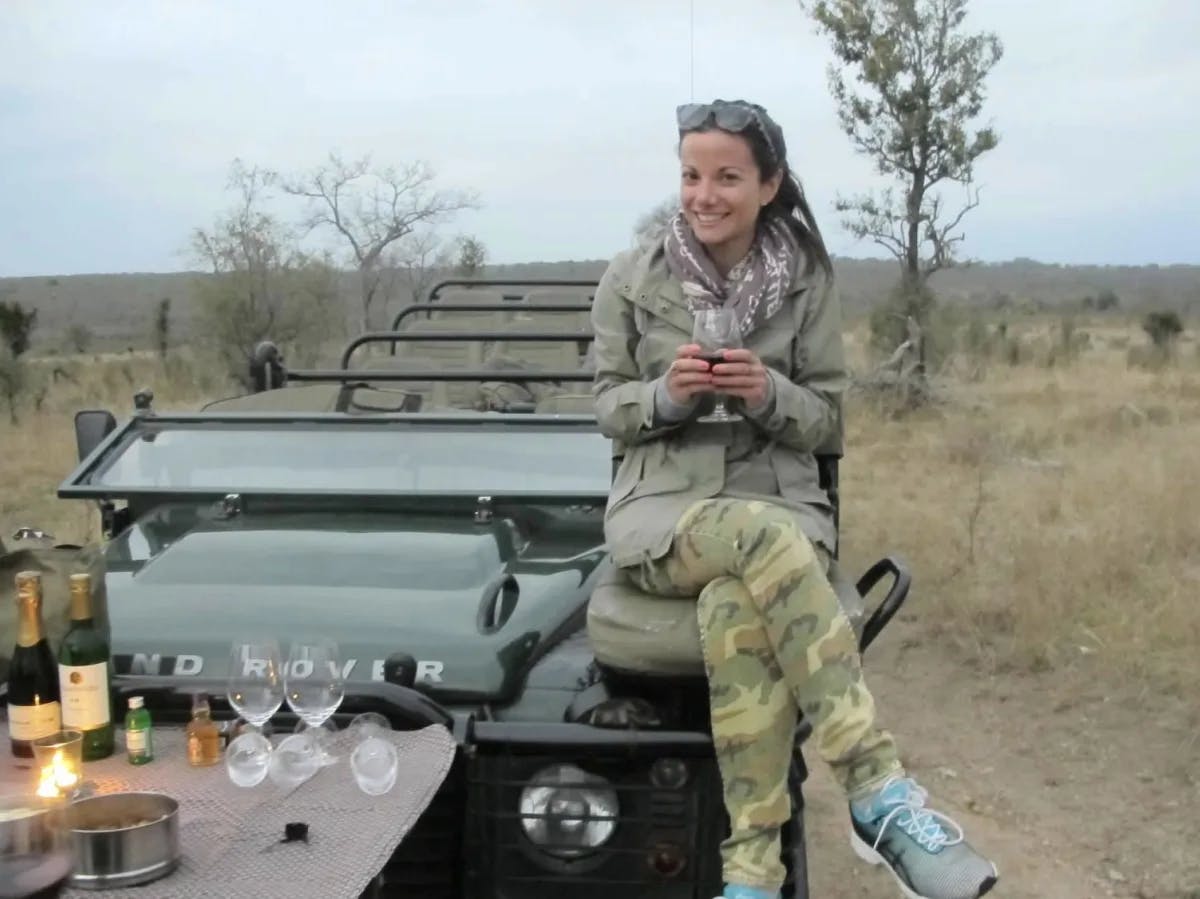 a woman in a green jacket holds a wine glass and sits on a jeep in the desert