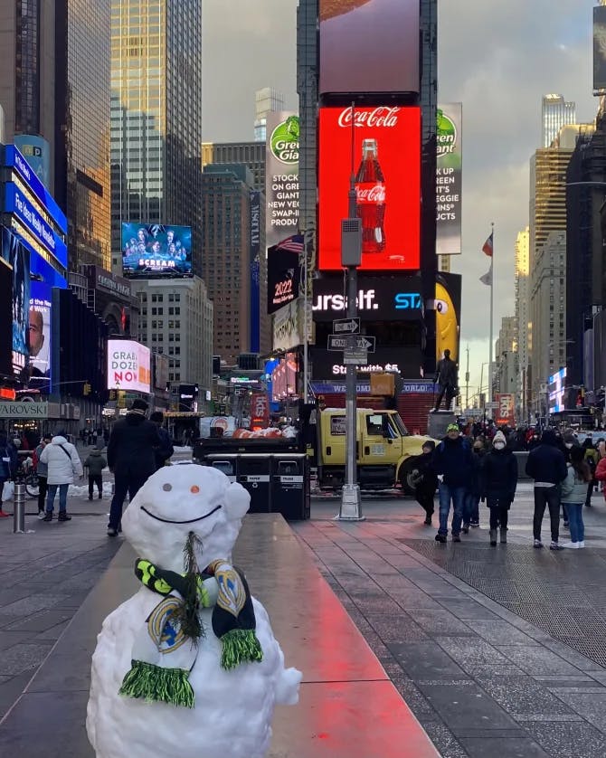 Picture of snowman at Times Square with all the lights in the background and a view of the city scape