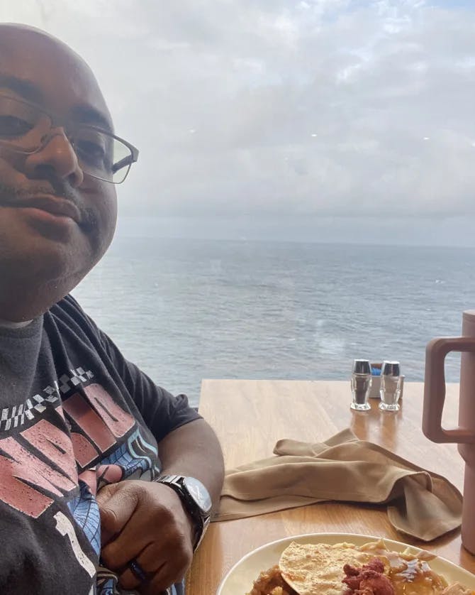 Mario posing for a selfie in front of a plate of food with the ocean in the background view.