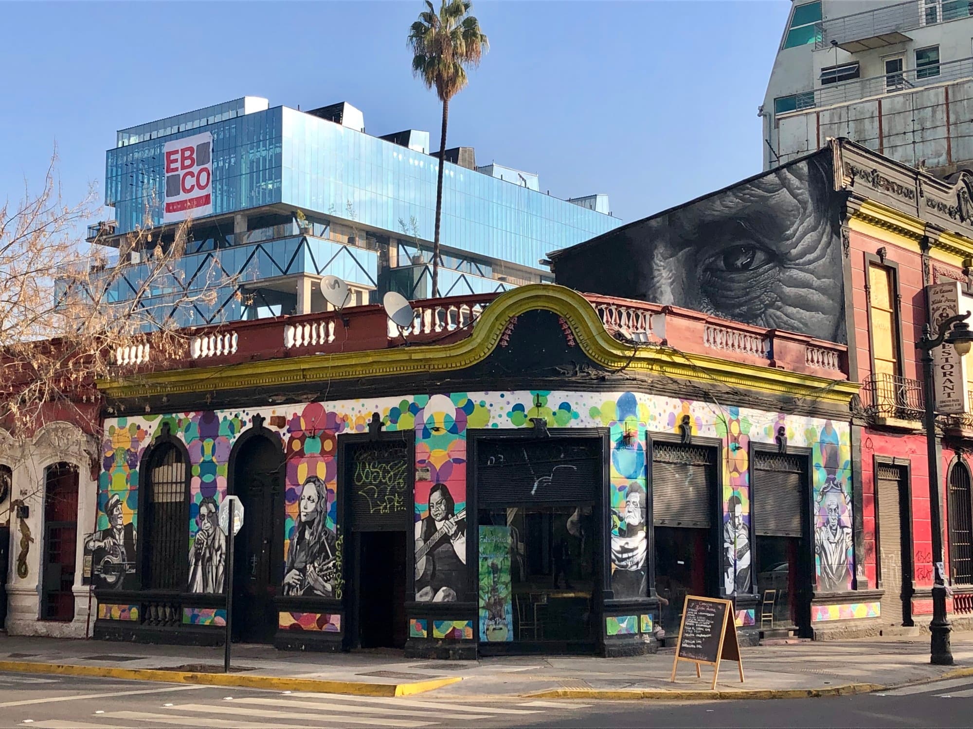 an old building with hand painted art on its facade with a palm tree and modern building behind it