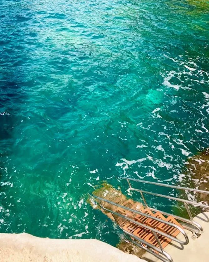 A beautiful view of turquoise water with a metal staircase leading into the water