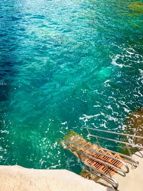 A beautiful view of turquoise water with a metal staircase leading into the water