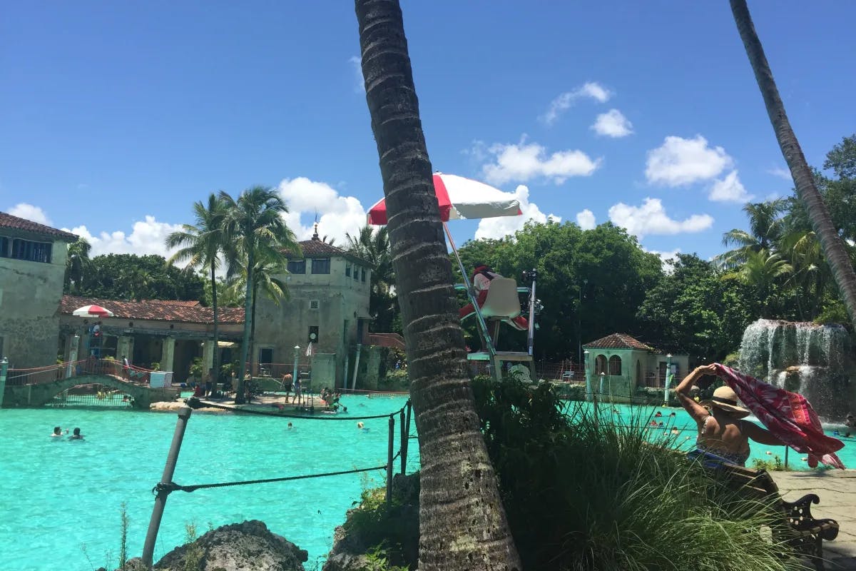 A picture of a hotel's poolside with people in it during the daytime