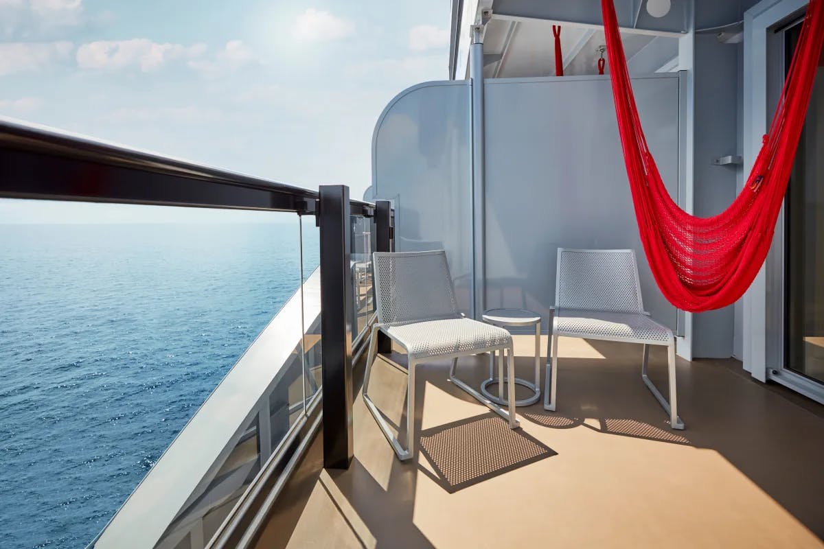 A cruise ships private deck with two white chairs and a red hammock. 