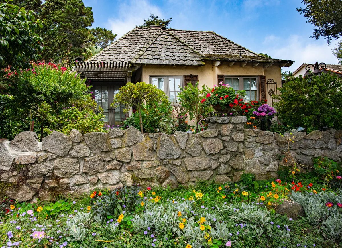 A cottage in Carmel with a rock wall and flowers.