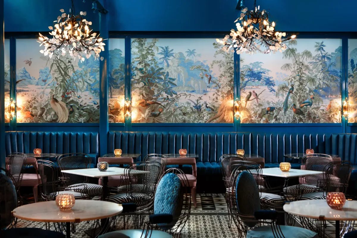 a dining room with blue banquettes, blue walls covered in vibrant wallpaper, and tables dotted with round lanterns