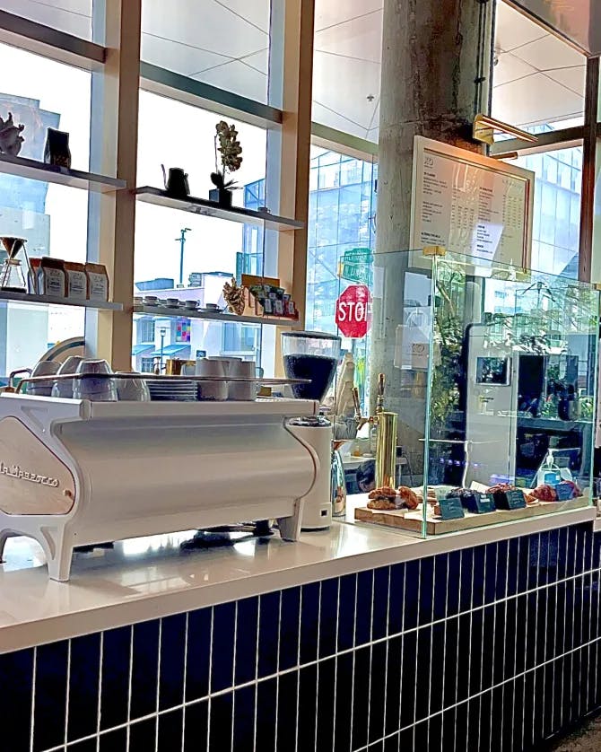 Picture of a coffee counter with navy blue subway tiles and an espresso machine in front a window looking out at the city