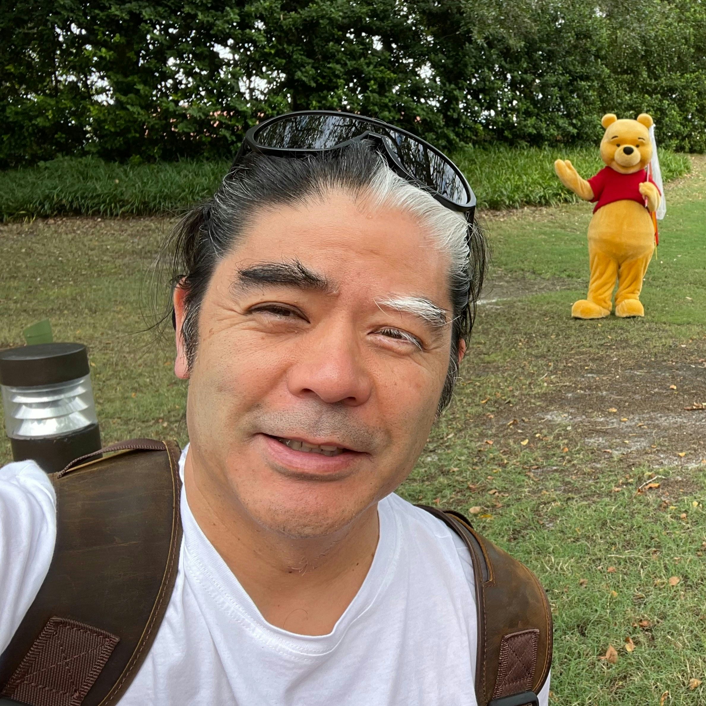 Travel Advisor Michael Kato with a white shirt and a yellow winnie the pooh bear standing behind him.