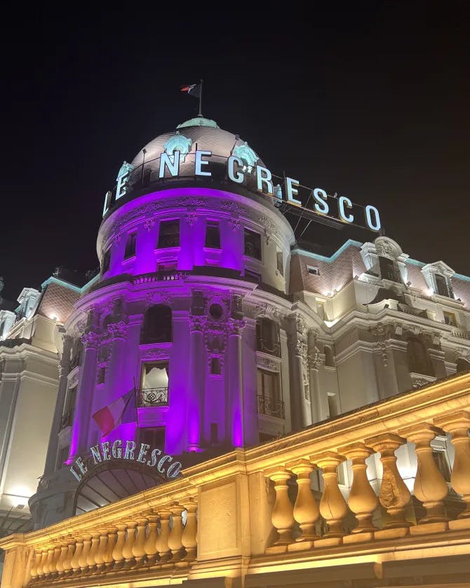 A picture of Le Negresco hotel lit up with a purple light at nighttime 
