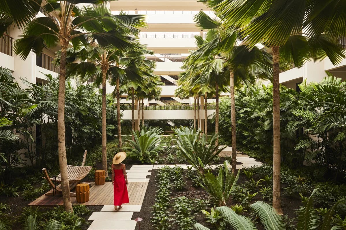 woman in red dress and sunhat walking in a hotel courtyard garden