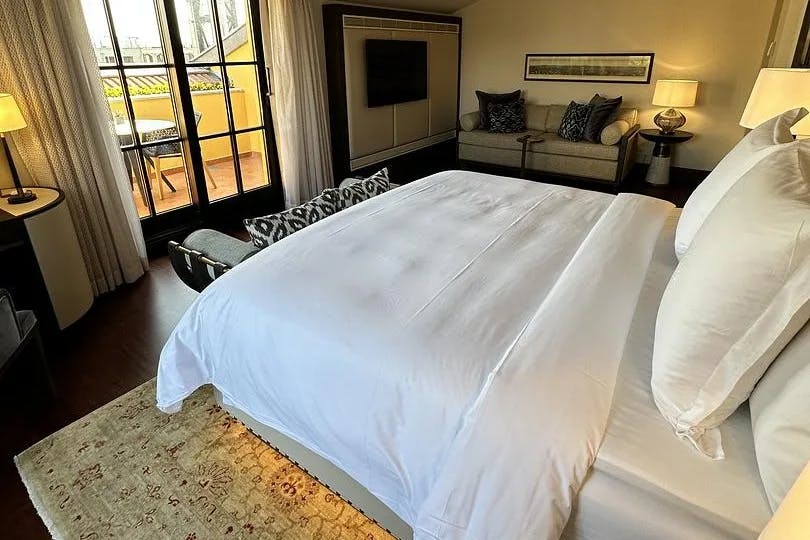 A bed with white sheets atop a tan and scarlet rug in a hotel room.