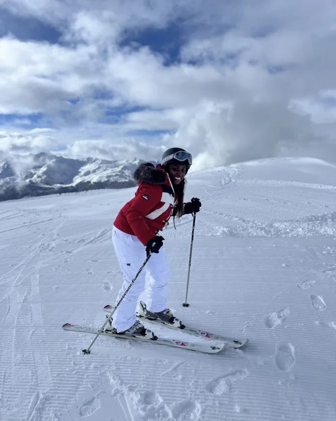Yasmir wearing a red jacket and white snow-pants skiing on a snowy mountain
