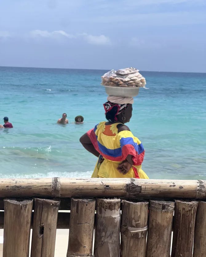 A street vendor carrying food items in a basket on her head on the beach