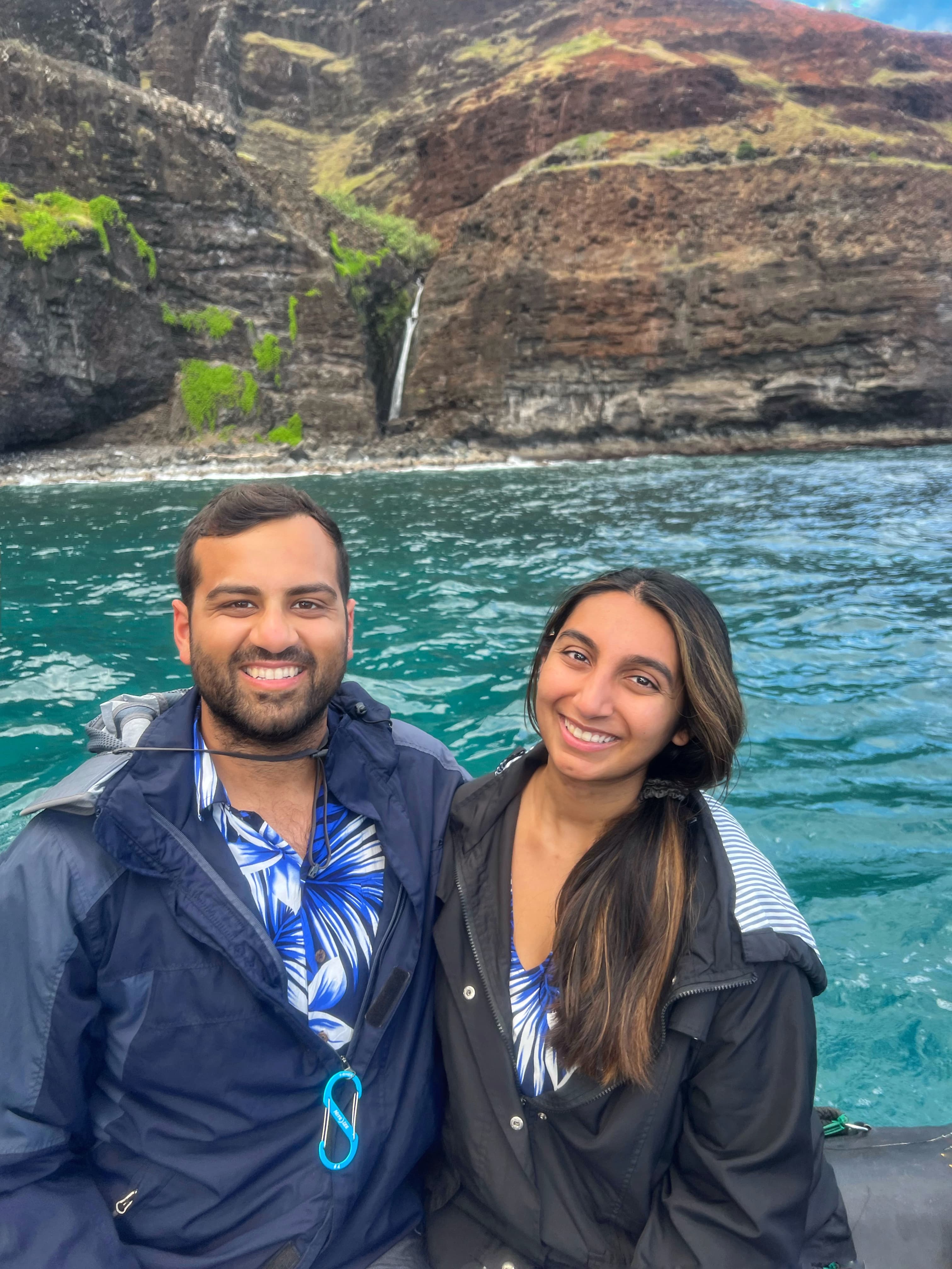 Khushbu and friend sitting and smiling on a boat with blue water and mountains in the background.