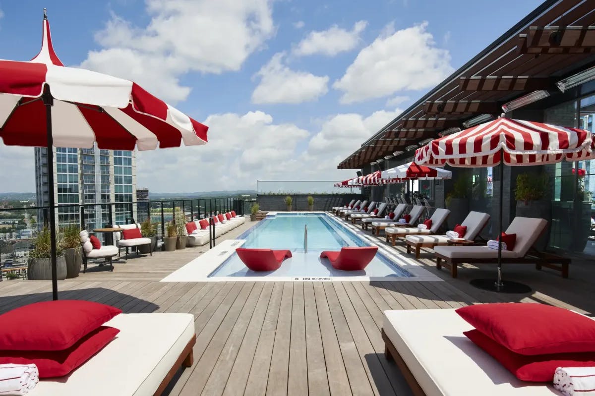 a rooftop pool surrounded by red lounge chairs and red-and-white striped umbrellas