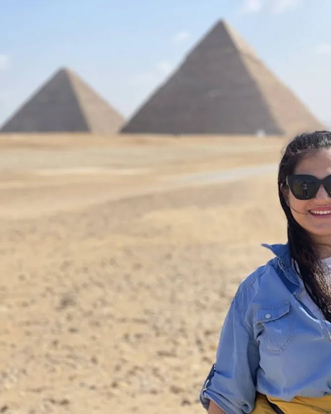 Mariela wearing a blue top and sunglasses standing in front of the Great Pyramids of Giza