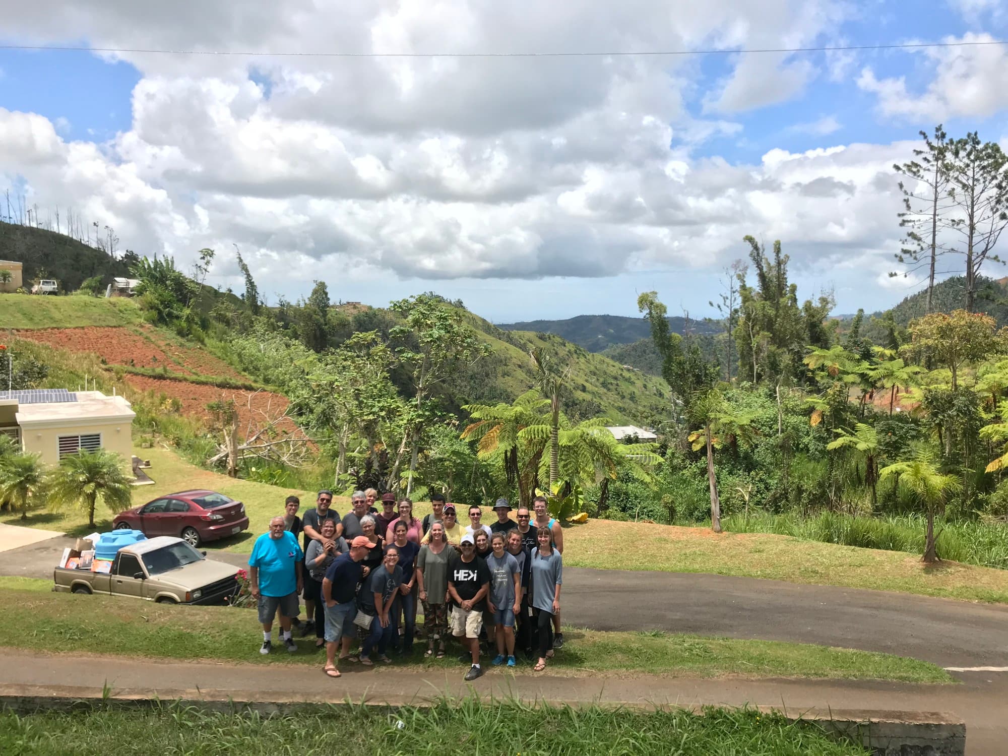 A group of people stand amid a lush jungly mountain landscape.