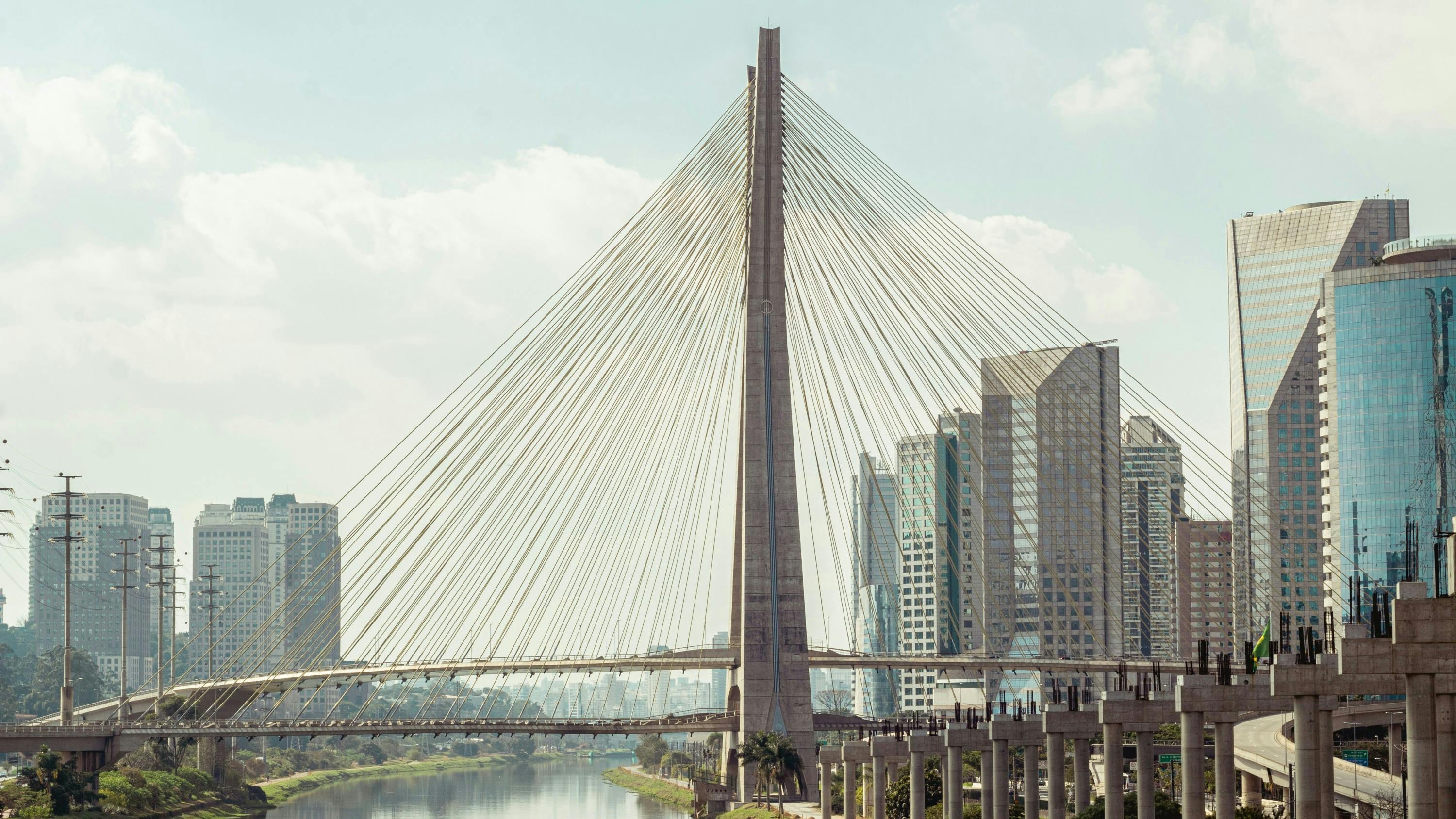 a modern bridge stretches across a river in a city on a sunny day