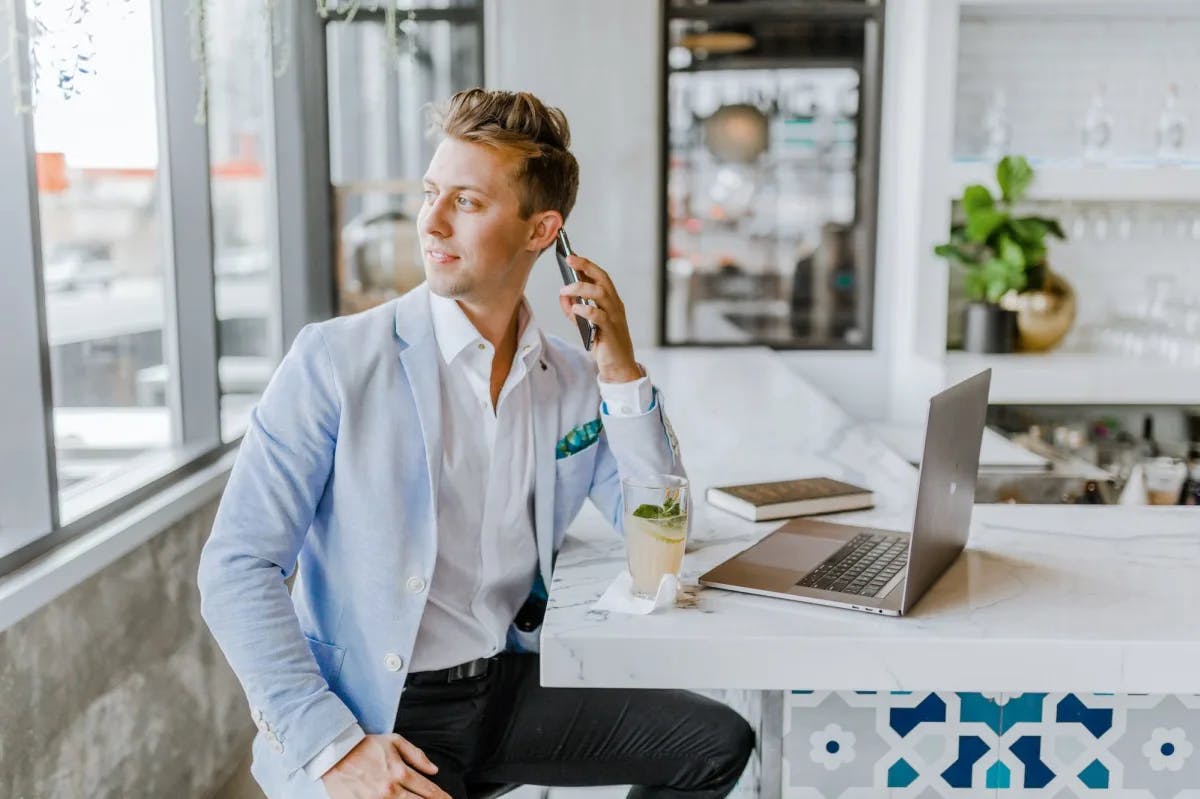 A man in a trendy contemporary suit chats on the phone while working from a remote office
