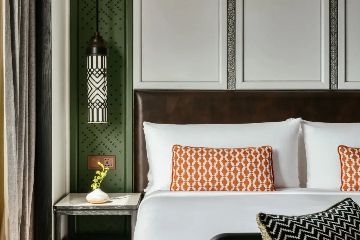 a close-up of a bed with orange pillows near a cylindrical black-and-white patterned lamp 