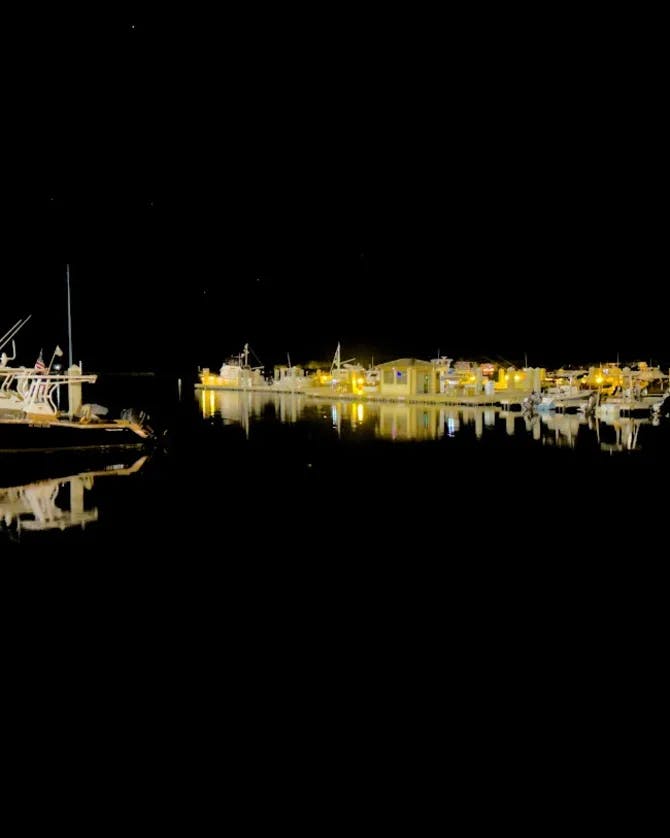 Boats docked in a harbor at nighttime with lights.
