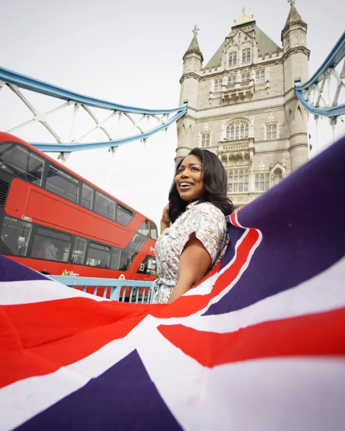 A woman stands near a British flag and a British red double-decker bus.