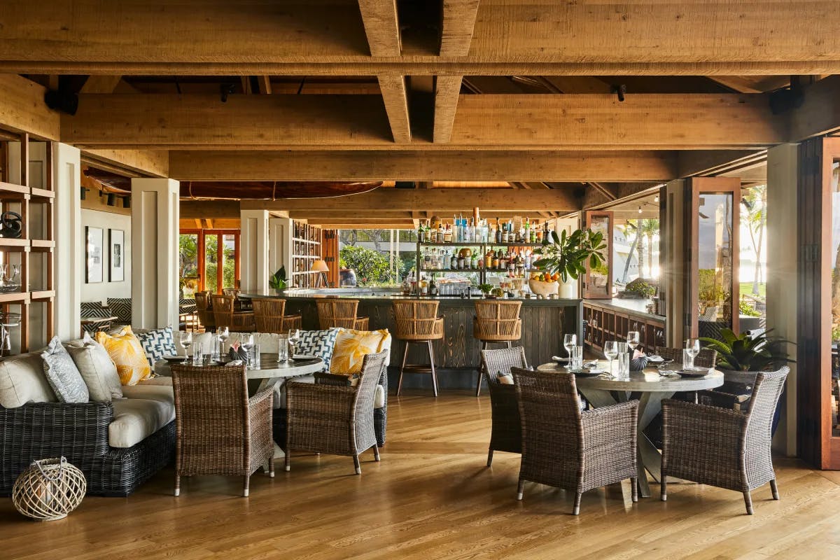 The Canoe House restaurant at Mauna Lani on the Island of Hawaii, with wicker furniture, a wood-beam ceiling and a bar.