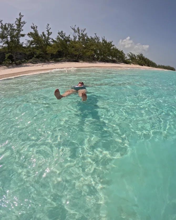 Picture of Jacob swimming in crystal clear water with the beach and trees in the background