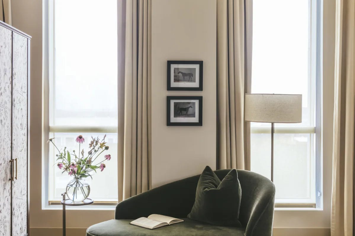 a green velvet chair near a window with white linen curtains
