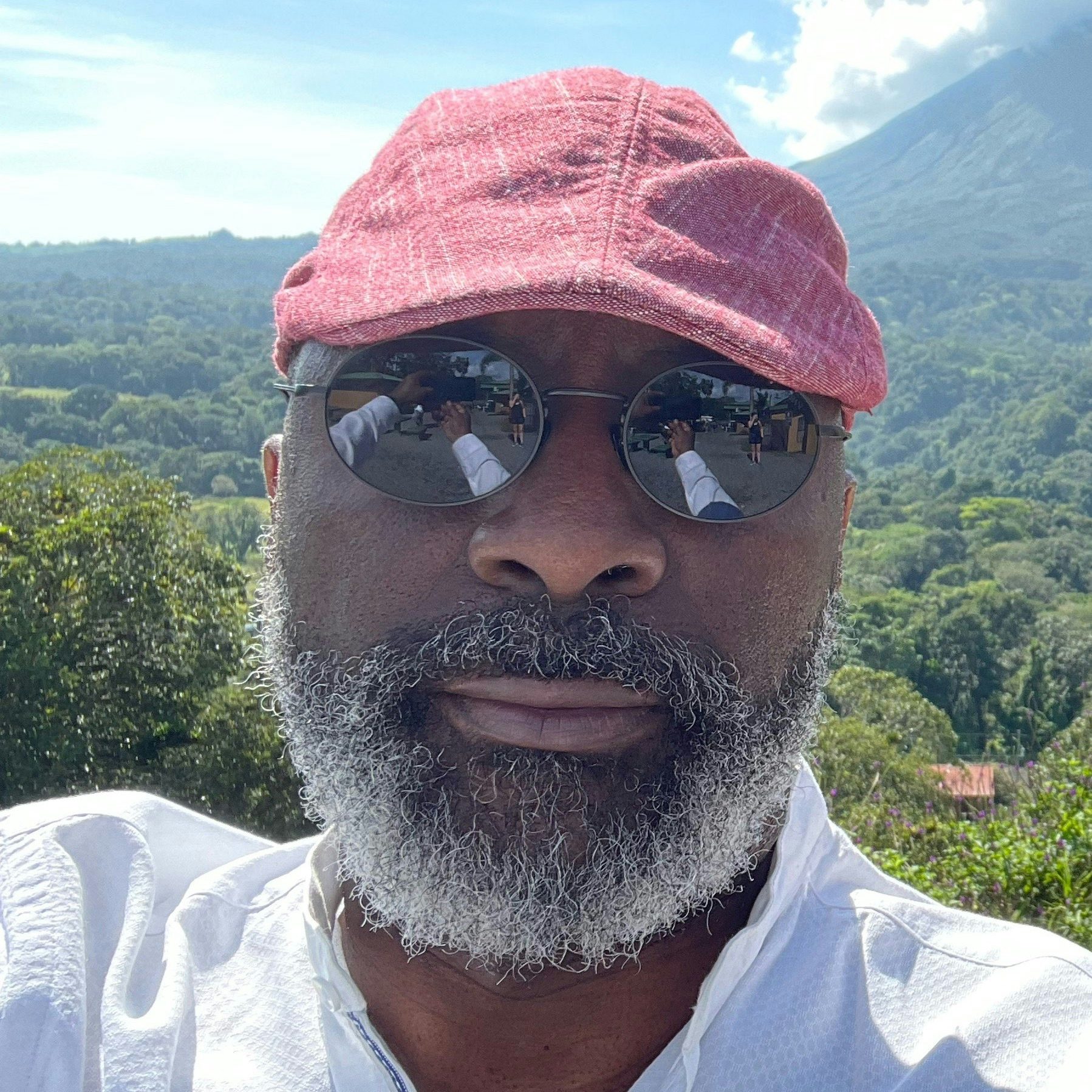 Travel Advisor Michel Sedrick Desir in a white shirt and red hat standing in front of green trees.