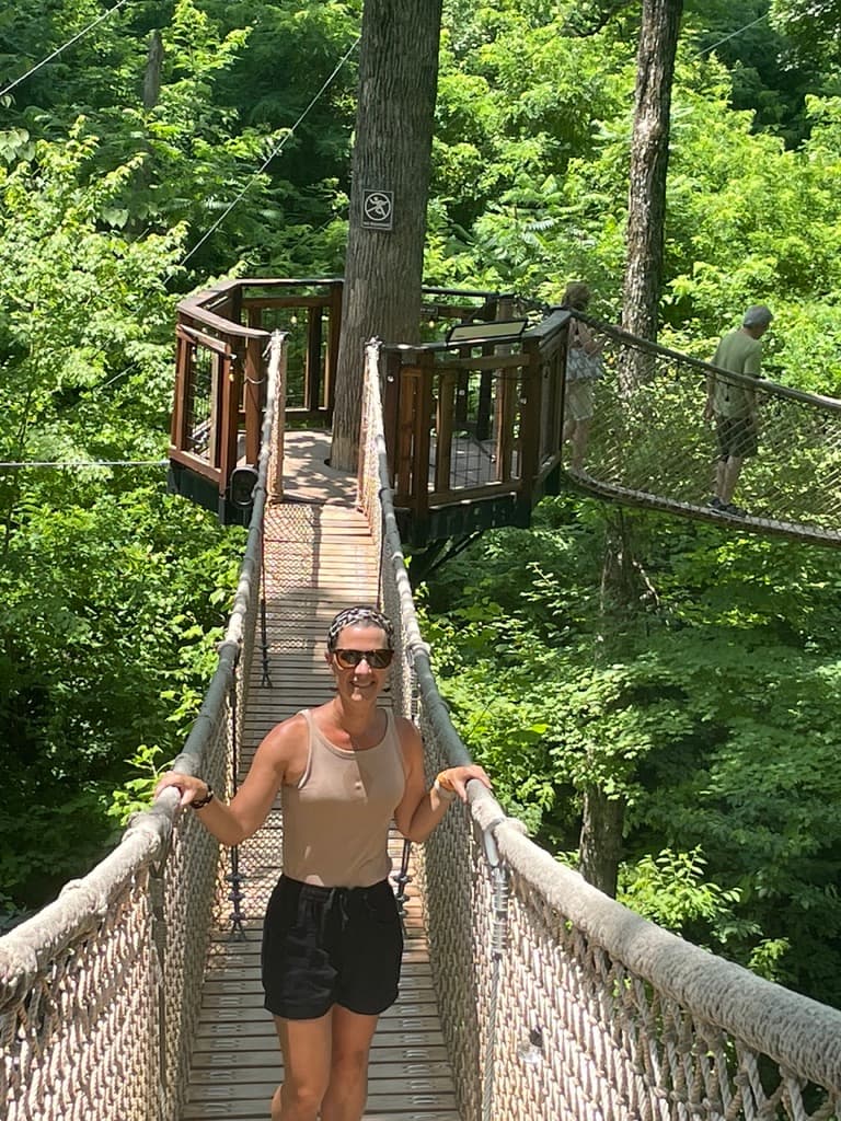 A woman standing on a narrow bridge between trees.