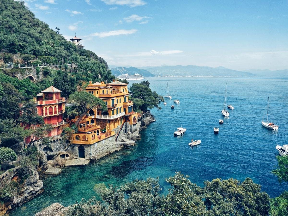 Sailboats in the blue waters and yellow and pink buildings along the coast of Italy in Portofino