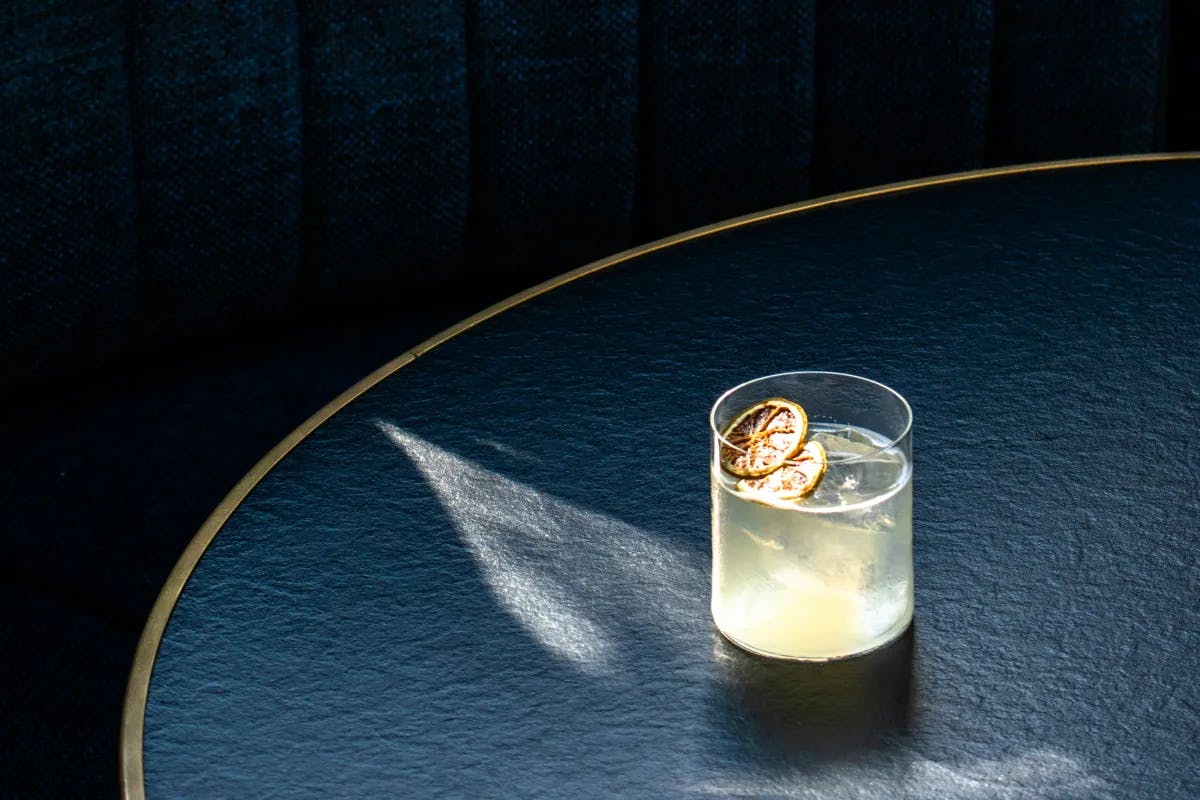 a small glass filled with yellow liquid sits on a round black table