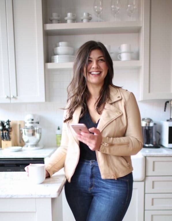 travel advisor Caitlin Bartram in a beige jacket and jeans standing in a kitchen