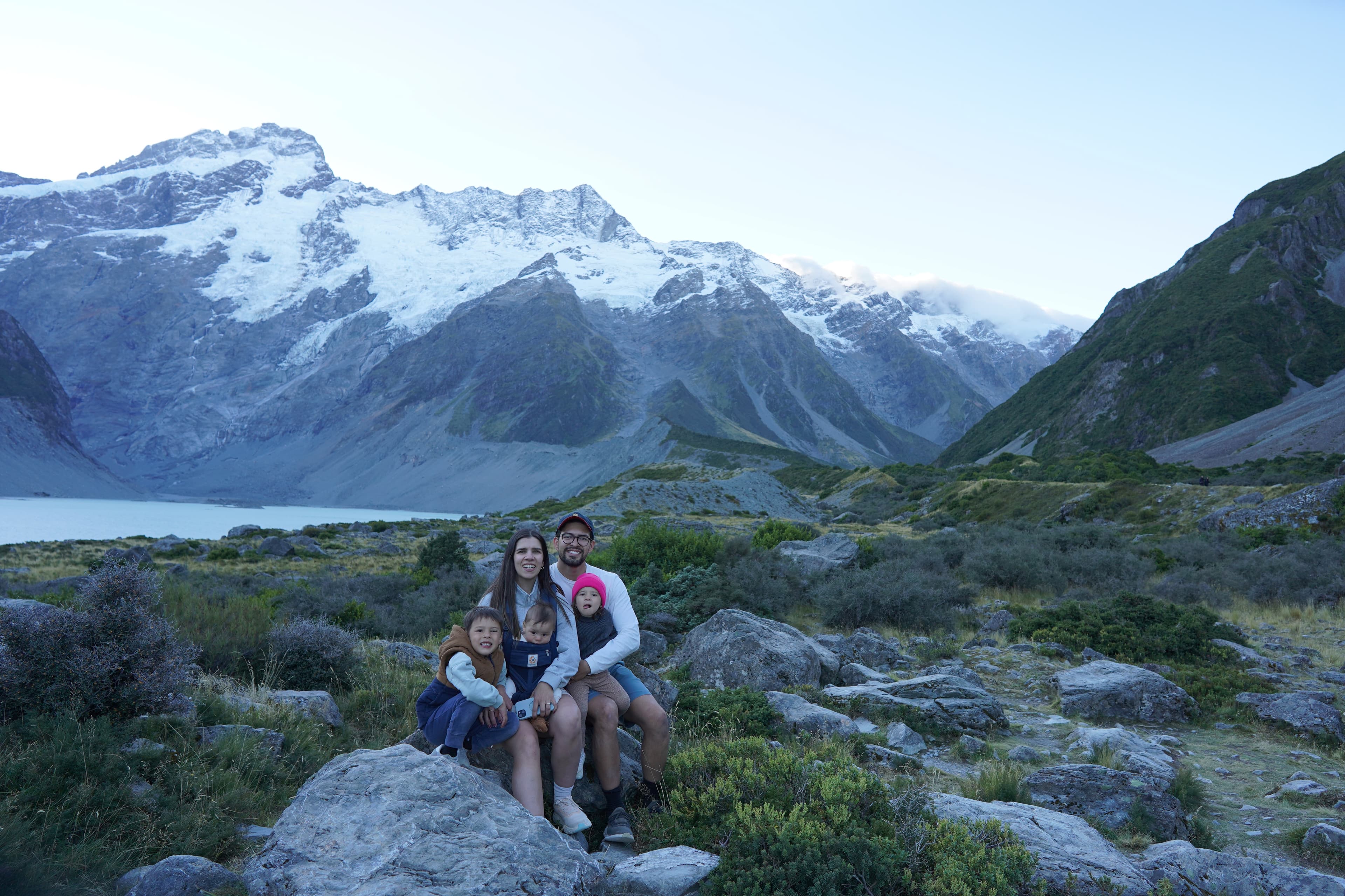 Maria, husband, and three kids sitting in front of snow-capped mountains at Aoraki / Mount Cook National Park in New Zealand.