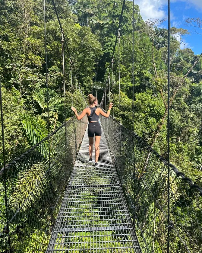 Picture of Shelby walking on the Místico Arenal Hanging Bridges surrounded by trees in the jungle