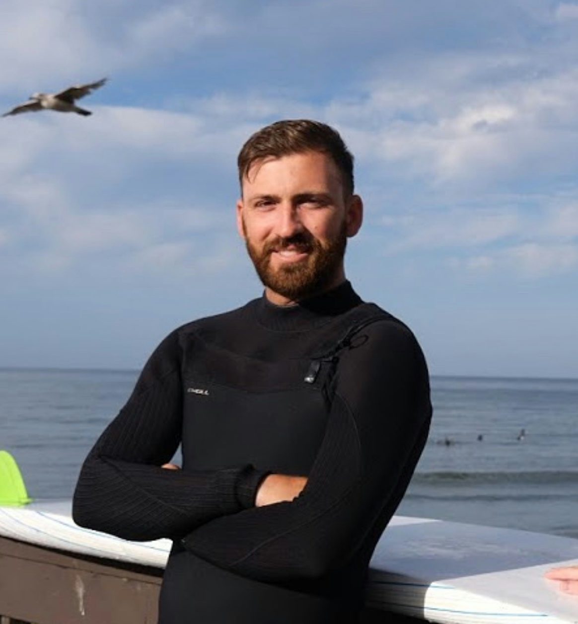 Travel Advisor Jake Adee in a wetsuit with a bird flying in the background and a large body of water.