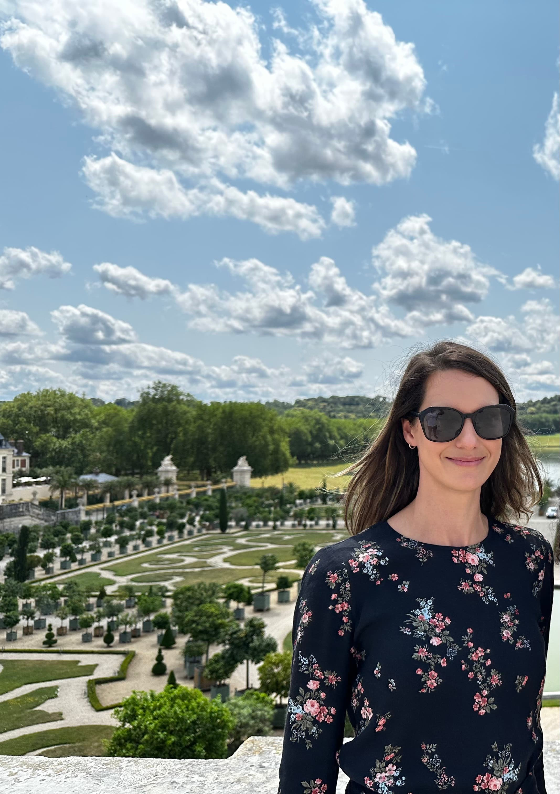 Kylie wearing a floral printed top and sunglasses while standing in front of a luxurious garden on a sunny day