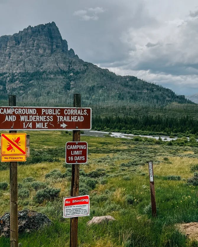 Picture of a campground sign in front of a mountain and grassy meadow