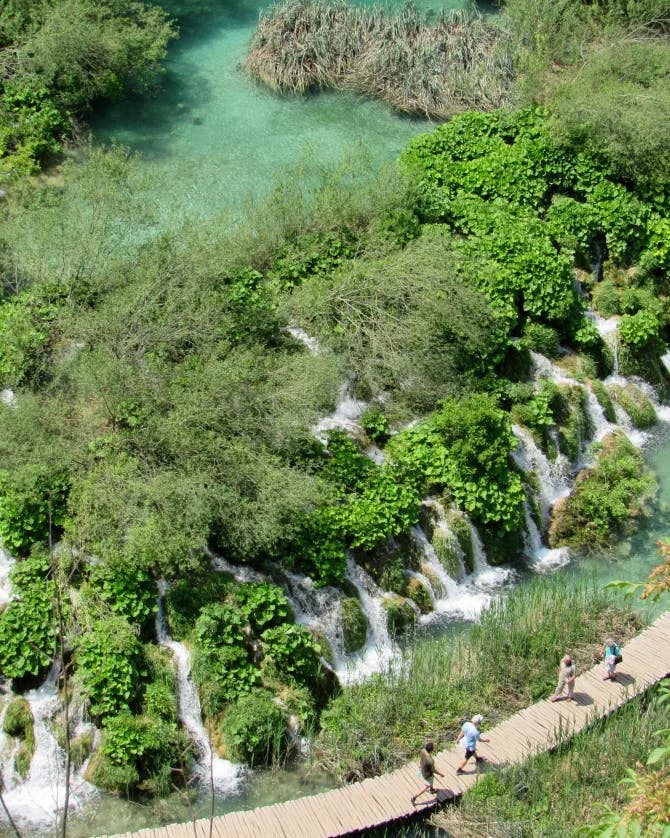 An aerial view of people walking along a trail at Plitvice Lakes National Park with trees and waterfalls in the surrounding areas